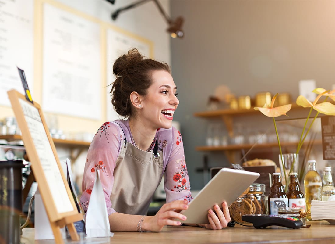 Business Insurance - Portrait of a Cheerful Young Small Business Owner Standing Behind the Front Counter of her Cafe While Holding a Tablet